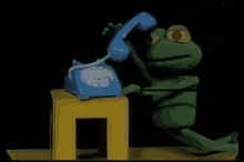 a green stuffed frog is talking on a blue telephone
