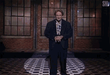 a man in a suit is standing in front of a brick wall with the letters snl on the bottom right