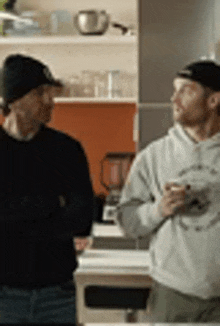 two men are standing next to each other in a kitchen drinking coffee .