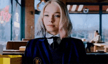 a girl in a school uniform and tie is sitting in a restaurant looking at the camera .