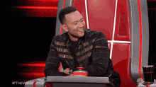 a man in a black jacket is sitting in a chair with a red button in front of him .