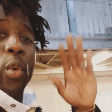 a man with dreadlocks is waving his hand in front of a window with the letter a on it