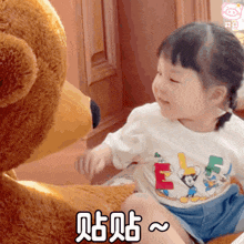 a little girl is sitting next to a teddy bear wearing a disney shirt