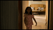 a little girl walking down a hallway with a couch behind her
