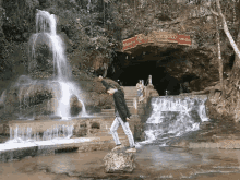 a man stands on a rock in front of a waterfall with a sign that says ' a ' on it