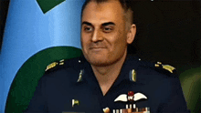 a man in a military uniform stands in front of a green and blue flag