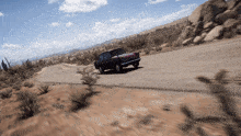 a car is driving down a desert road with mountains in the background