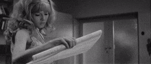 a black and white photo of a woman reading a book .