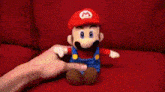 a person is holding a stuffed mario toy on a red couch .