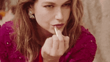 a woman in a pink top is applying lipstick on her lips