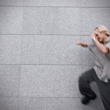 a man in a grey shirt and gray pants is standing in front of a gray wall