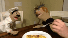 two puppet chefs are sitting at a table with a plate of food in front of them