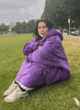 a woman wearing a purple sweatshirt sits on the grass