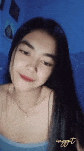 a woman with long black hair is wearing a blue tank top and a necklace with the word inggit written on the bottom