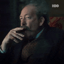 a man with a mustache is smoking a cigar in front of an hbo logo