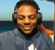 a man wearing headphones and a blue hoodie is smiling with his eyes closed
