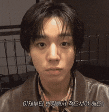 a young man wearing a brown leather jacket and a plaid shirt is looking at the camera