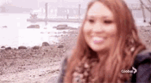 a woman is standing on a rocky beach with a pink bubble gum in her mouth .
