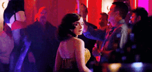 a woman in a dress is standing in a crowd of people in a dark room .