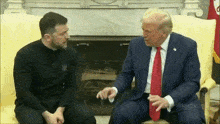 two men in suits and ties are sitting on a couch and talking to each other