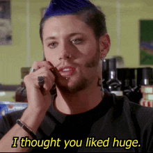 a man with a blue mohawk is talking on a cell phone and the caption says i thought you liked huge