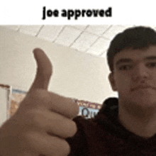 a young man is giving a thumbs up sign in front of a wall .