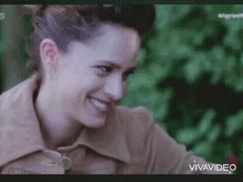a woman in a brown jacket is smiling and looking at the camera in a video .