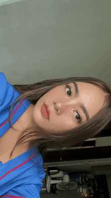 a woman in a blue shirt takes a selfie with a fan in the background