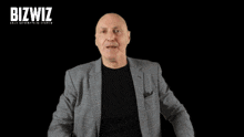 a bald man in a suit holds a piece of paper in front of a bizwiz lead generation system sign