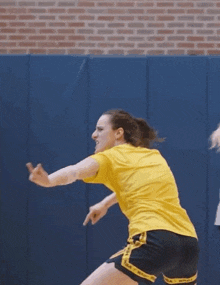 a woman in a yellow shirt and black shorts that say ncaa on them