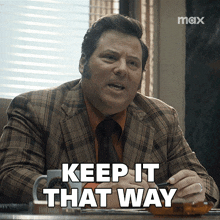 a man in a plaid suit and tie is sitting at a desk and says keep it that way