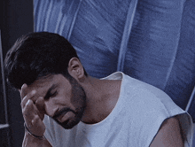 a man with a beard wearing a white shirt holds his head