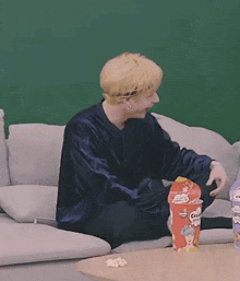 a man is sitting on a couch holding a box of pringles .