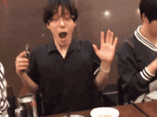 a man sitting at a table with his mouth open and his hands up