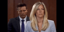 a man and a woman are sitting in a courtroom . the woman is wearing a blue jacket and a blue tie .