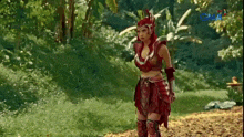 a woman in a red warrior costume is standing in the grass .