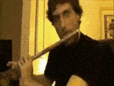 a man in a black shirt is playing a flute in a room