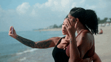 two women are taking a selfie on the beach and one has a tattoo on her arm that says ' i love you '