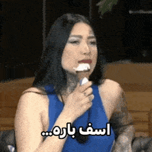a woman in a blue tank top is eating an ice cream cone with arabic writing on it