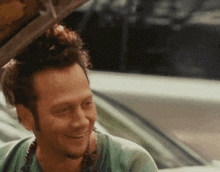 a man with a bun on his head is smiling in front of a white car