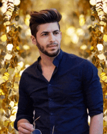 a man in a blue shirt is holding a pair of sunglasses in front of a gold background