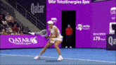 a woman is playing tennis in front of a qatar advertisement
