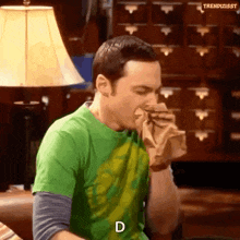 a man in a green shirt is blowing his nose while eating a hamburger .