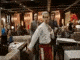 a man in a white shirt and red pants is dancing in a room with people .