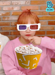 a girl wearing 3d glasses holds a bucket of popcorn in her hand
