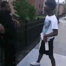 two men are standing next to each other on a sidewalk and talking .