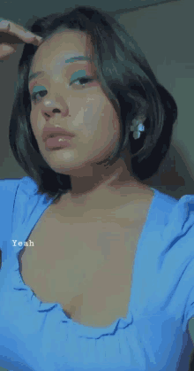 a woman wearing a blue top with a flower earring is taking a picture of herself .