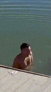 a shirtless man is standing in the water near a wooden dock