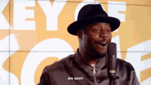 a man wearing a hat and jacket is talking into a microphone and says oh shit