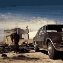 a man is standing next to a car in a dirt field